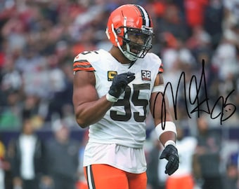 May include: An American football player in a white and orange uniform, wearing a helmet with a black facemask. The jersey has the number 35 in large black numerals. The player is on a field with a crowd in the background.
