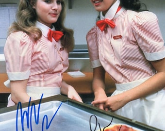 May include: A glossy photograph featuring two individuals wearing matching uniforms consisting of short-sleeved, white and red vertically striped shirts with white collars, red bow ties, and white aprons, positioned behind a rectangular pizza.