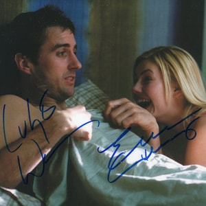 May include: A couple in bed, the woman is laughing and the man is looking at her. The man has signed his name "Luke Wilson" and the woman has signed her name "Eva Mendes".