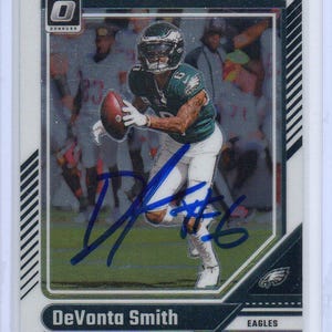 May include: A football trading card featuring DeVonta Smith of the Eagles. The card has a photo of Smith in action, wearing a green and white uniform, holding a football. The card is signed and has the Optic Donruss logo.