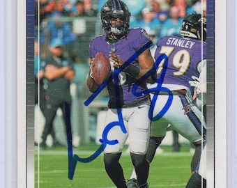 May include: A football trading card featuring Lamar Jackson of the Baltimore Ravens in a purple uniform, holding a football. The card has a blue border and the Score logo. The player's signature is visible.