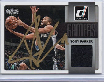 May include: A basketball trading card featuring Tony Parker of the San Antonio Spurs. The card has a photo of Parker in action, with his autograph in gold. The card also includes a patch of black fabric.