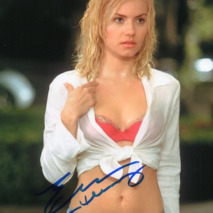 May include: A woman with wet blonde hair wearing a white button-down shirt tied at the waist, revealing a red bra. She is also wearing blue jeans. The image has a signature in blue ink.