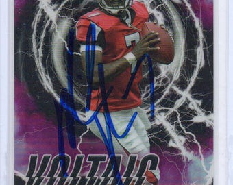May include: A Michael Vick football card with a purple and white lightning design. The card features a player in a red and black uniform holding a football. The word "VOLTAIC" is printed in white, and the card is signed in blue.