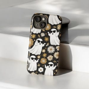 Pode incluir: Uma capa de telefone preta com um padrão de fantasmas brancos usando óculos de sol e flores douradas.