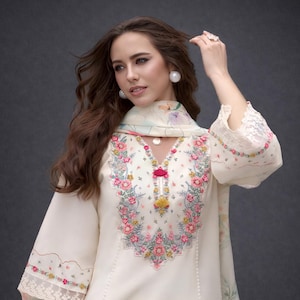 Può includere: Set tunica e sciarpa ricamati color crema. La tunica presenta un design floreale in rosa, verde e giallo intorno allo scollo e alle maniche. La sciarpa ha una stampa floreale abbinata. Le maniche hanno finiture in pizzo.