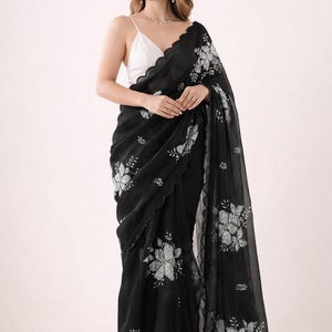 May include: Black saree with floral embroidery. The saree features a scalloped edge and is paired with a white top. The floral design is in a contrasting color, creating a striking visual effect. The saree is draped elegantly.