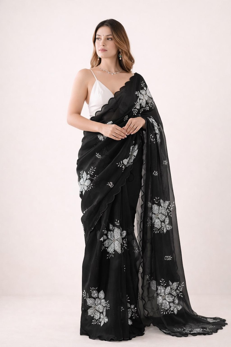 May include: Black saree with floral embroidery. The saree features a scalloped edge and is paired with a white top. The floral design is in a contrasting color, creating a striking visual effect. The saree is draped elegantly.