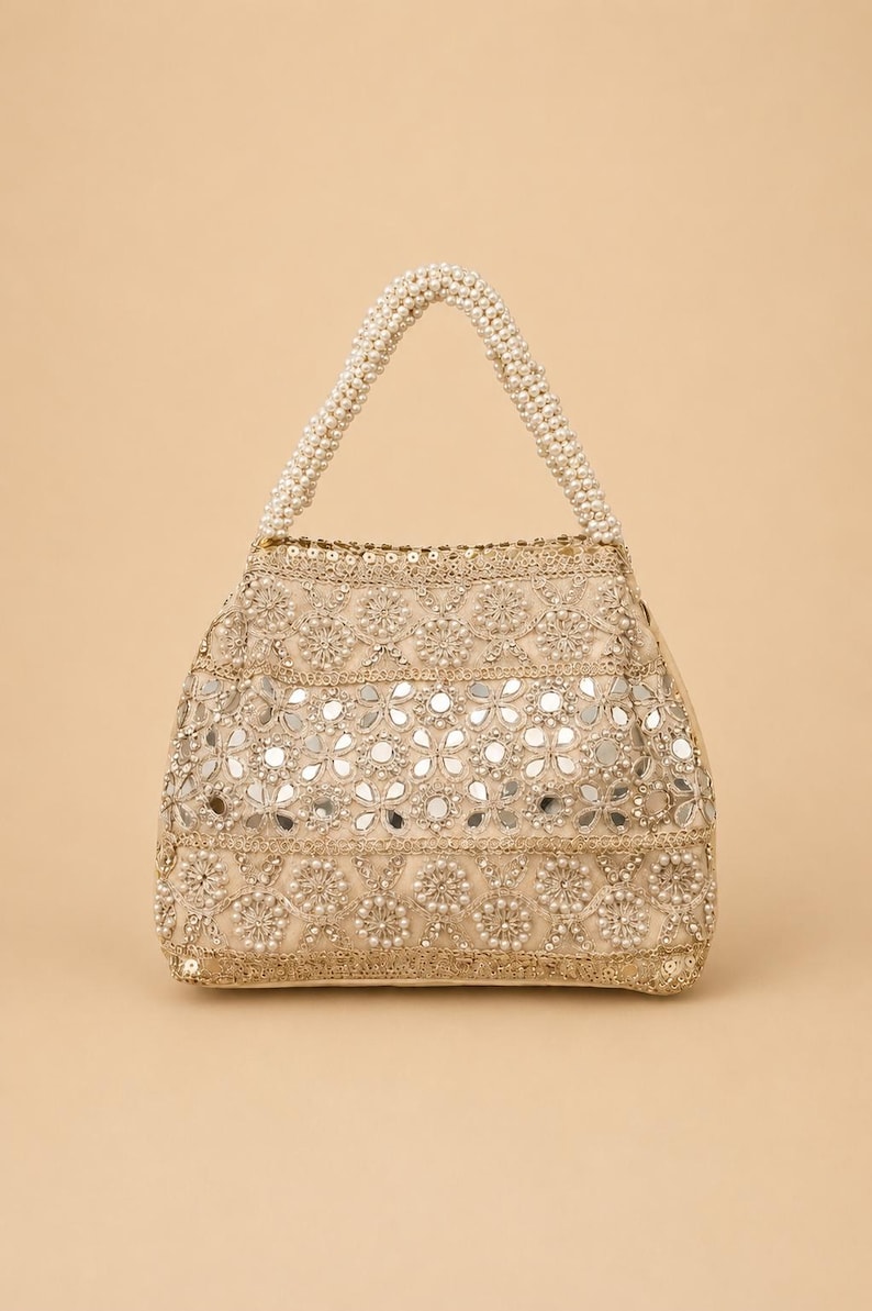 K&ouml;nnte beinhalten: Beige Handtasche mit Perlenhenkel. Die Tasche ist mit aufwendigen Blumenmustern, kleinen Spiegeln und perlenartigen Perlen verziert. Der Griff besteht aus eng aufgereihten wei&szlig;en Perlen.