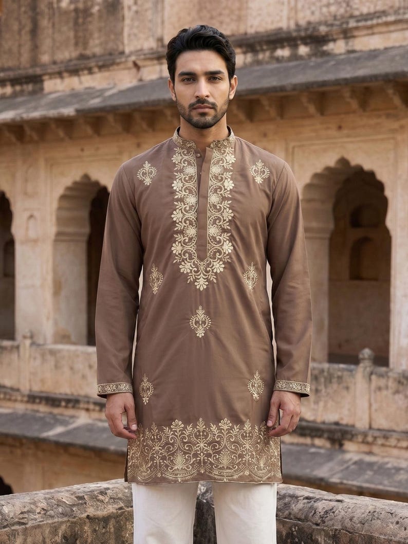 K&ouml;nnte beinhalten: Ein lang&auml;rmeliger brauner Kurta mit aufwendiger goldener Stickerei entlang des Stehkragens, der Knopfleiste und des Saums. Das Kleidungsst&uuml;ck hat eine gerade Silhouette mit einem gekn&ouml;pften Ausschnitt und passenden goldenen Blumenmustern.