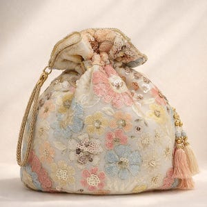 May include: A cream-coloured drawstring bag with embroidered pastel flowers and sequins. The bag features a gold-coloured handle and tassel accents in shades of pink and gold. The floral design includes pink, blue, and yellow blossoms.