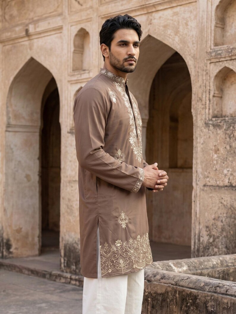 K&ouml;nnte beinhalten: Ein lang&auml;rmeliger brauner Kurta mit aufwendiger cremefarbener Stickerei entlang des Stehkragens, der Knopfleiste, der &Auml;rmelb&uuml;ndchen und des unteren Saums, kombiniert mit einer schlichten wei&szlig;en Hose.