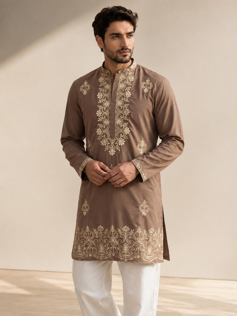 K&ouml;nnte beinhalten: Ein lang&auml;rmeliger, taupefarbener Kurta mit aufwendigen, hellen Stickereien entlang des Stehkragens, der mittleren Knopfleiste, an den Manschetten und am unteren Saum, kombiniert mit einer schlichten wei&szlig;en Hose.