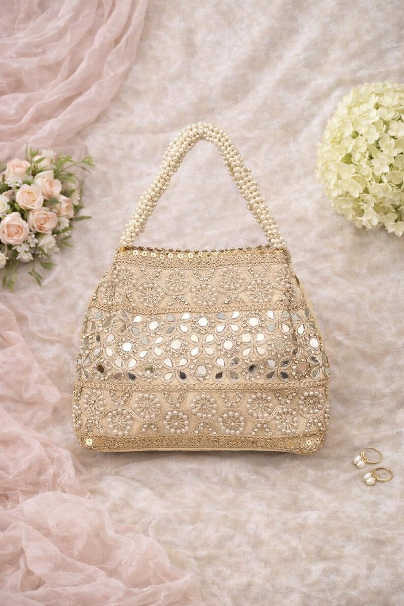K&ouml;nnte beinhalten: Beige Handtasche mit perlenbesetztem Griff und aufwendiger Stickerei. Die Tasche ist mit kleinen Spiegeln und Perlen verziert, was einen schimmernden Effekt erzeugt. Die Tasche ist ca. 25 cm breit und 20 cm hoch.