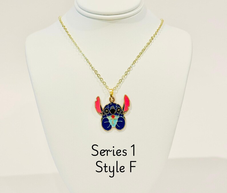 K&ouml;nnte beinhalten: Goldkette mit einem blauen Stitch-Charakter-Anh&auml;nger. Der Anh&auml;nger hat rosa Ohren und einen blauen K&ouml;rper mit einem hellblauen Herzen. Der Text "Series 1 Style F" befindet sich unter dem Anh&auml;nger.