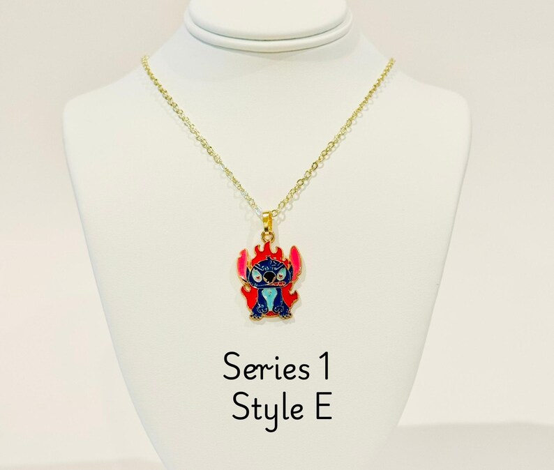 K&ouml;nnte beinhalten: Goldkette mit einem blauen und roten Emaille-Anh&auml;nger mit Stitch. Der Anh&auml;nger zeigt Stitch mit Flammen um ihn herum. Der Text "Series 1 Style E" ist unter dem Anh&auml;nger gedruckt.