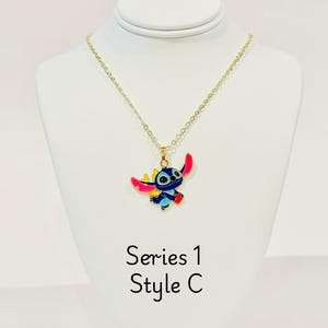K&ouml;nnte beinhalten: Goldkette mit einem blauen, rosa und gelben Stitch-Charakter-Anh&auml;nger. Der Anh&auml;nger ist eine Zeichentrickfigur des Charakters aus dem Disney-Film Lilo & Stitch. Die Kette ist mit "Serie 1 Style C" gekennzeichnet.