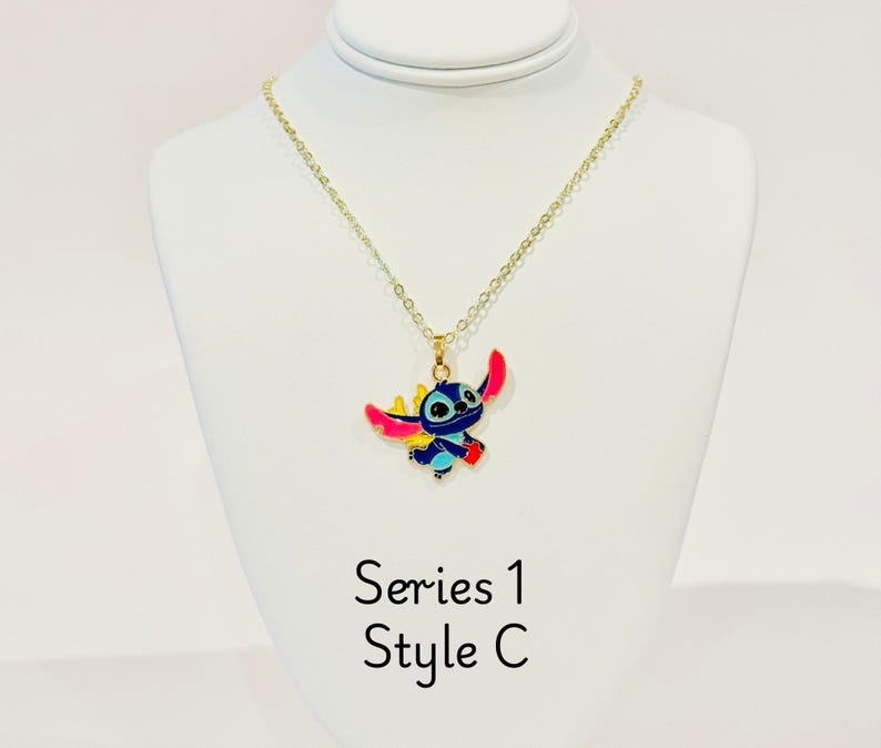 K&ouml;nnte beinhalten: Goldkette mit einem blauen, rosa und gelben Stitch-Charakter-Anh&auml;nger. Der Anh&auml;nger ist eine Zeichentrickfigur des Charakters aus dem Disney-Film Lilo & Stitch. Die Kette ist mit "Serie 1 Style C" gekennzeichnet.