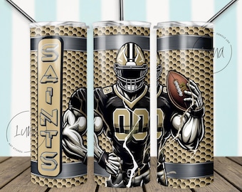 Puede incluir: Un vaso dorado y negro con un jugador de fútbol americano que lleva una camiseta de los Saints y sostiene un balón de fútbol. El vaso tiene un patrón de panal y la palabra "Saints" está impresa en el lateral.