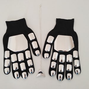 Puede incluir: Un par de guantes negros con placas de metal plateadas en los dedos y la palma. Un colgante plateado cuelga de una cadena.