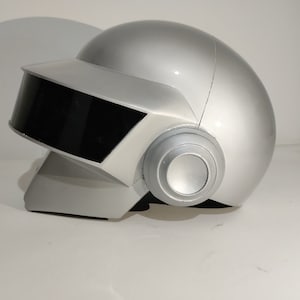 May include: A silver helmet with a black visor and a silver earpiece. The helmet is designed to look like a robot's head.