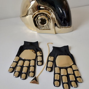 Può includere: Un casco dorato e nero con una catena e un ciondolo dorati. Il casco ha una visiera nera e dettagli dorati. I guanti sono neri con dettagli dorati.