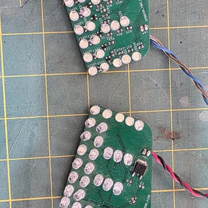 Peut inclure: Deux circuits imprimés verts avec plusieurs lumières LED et composants électroniques. Les cartes sont connectées à des fils et sont sur une surface de grille verte. L'image est prise d'en haut.