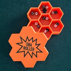 Puede incluir: Rodillo de dados hexagonal naranja con el texto "OBA ROLLER" en negro. El rodillo está abierto, revelando varios dados en compartimentos individuales. Los dados son blancos con puntos negros. Una flecha apunta hacia arriba en un compartimento.
