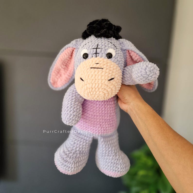 Pode incluir: Um brinquedo de pel&uacute;cia artesanal do Eeyore, o burro de Winnie the Pooh. O brinquedo &eacute; principalmente lavanda com uma barriga e orelhas rosa, um focinho bege e um tufo de cabelo preto. O brinquedo &eacute; macio e fofinho.