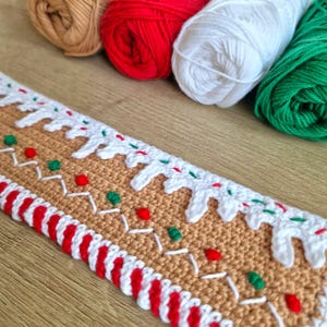 May include: A crocheted gingerbread house trim with white icing, red and green candy, and a red and white candy cane border.