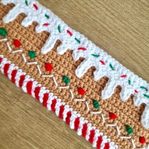 May include: A crocheted gingerbread house trim with white icing, red and green candy, and a red and white candy cane border.