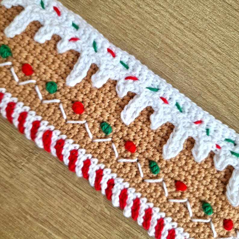 May include: A crocheted gingerbread house trim with white icing, red and green candy, and a red and white candy cane border.