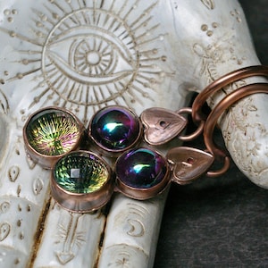 May include: A pair of copper-toned earrings featuring two round, faceted stones each. One stone in each earring displays a vibrant, iridescent green and yellow finish, while the other stone shows a deep, dark purple and blue iridescent sheen.
