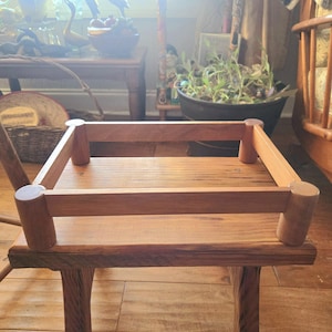 May include: A wooden tray with a rectangular shape and rounded edges. The tray is made of light brown wood and has a natural finish. The tray is sitting on a wooden table.