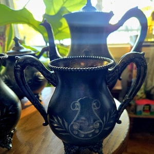 May include: A set of antique silver tea service pieces, including a teapot, creamer, and sugar bowl. The pieces are all decorated with intricate floral designs and have a dark, aged patina.