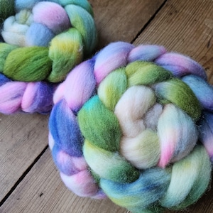 Puede incluir: Dos haces trenzados de lana cardada suave con una paleta de colores variados en rosa pastel, lavanda, azul cielo, verde lima y crema. Las fibras están densamente compactadas y retorcidas en bobinas gruesas y redondeadas con textura mate.
