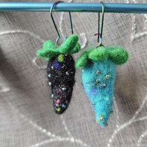 May include: A pair of handmade felt strawberry earrings. One earring is black with colorful bead accents, the other is turquoise with silver bead accents. Both have green felt leaves and are suspended from silver-colored ear wires.