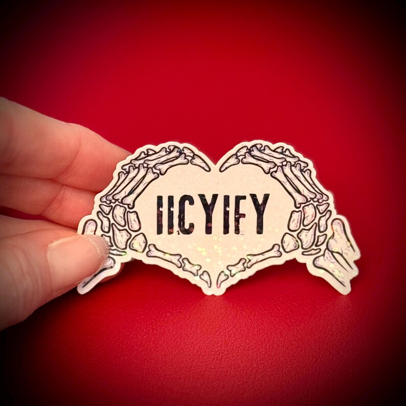 May include: A heart-shaped sticker with a skeleton hand design. The hands form the shape of a heart, with the word "HCYIFY" in the center. The sticker has a holographic, glittery finish and is set against a red background.
