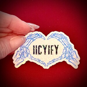May include: A holographic sticker in the shape of a heart, featuring blue skeletal hands forming the heart shape. The sticker has the word "IICYIFY" in black block letters in the center. The background is a solid red.