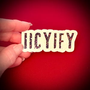 May include: A rectangular sticker with the word "IICYIFY" in black letters filled with glitter. The sticker has a white border and is held against a red background.