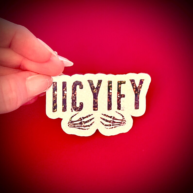 May include: A white sticker with the word "ICYIFY" in black letters with glitter accents and two skeleton hands. The sticker is held against a red background.