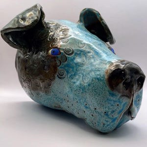 May include: A ceramic dog head sculpture with blue and brown glaze. The dog has blue eyes and a textured surface.
