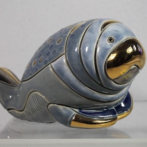 May include: A blue and gold ceramic figurine of a manatee. The figurine has a detailed, textured surface and a stylized design.
