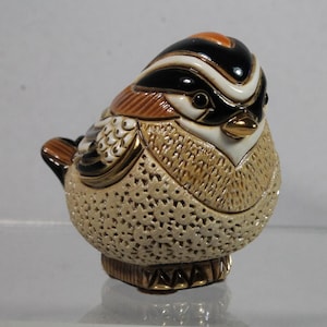 May include: A small ceramic bird figurine with a detailed design. The bird is brown, white, black, and gold with a textured surface.