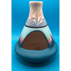 May include: A conical ceramic incense burner featuring a wide teal base and a large arched opening. The upper section is painted in light blue and tan with etched geometric patterns, while the sides display painted silhouettes of pine trees.