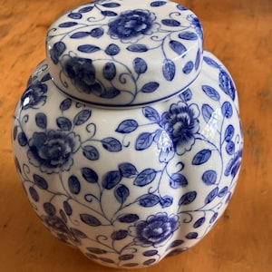 May include: A white ceramic jar with a lid, adorned with a blue floral pattern. The jar has a rounded shape with a slightly textured surface. The lid mirrors the floral design, creating a cohesive decorative piece. The jar is likely used for storage or display.
