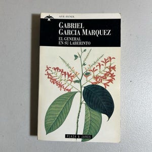 May include: A paperback book titled "EL GENERAL EN SU LABERINTO" by Gabriel Garcia Marquez. The cover features a botanical illustration of a plant with green leaves and red flowers. The publisher's name, Plaza & Janes, is at the bottom.