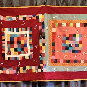 May include: A handmade quilt with a patchwork design. The quilt features a red background with colourful squares and a white border. The quilt is decorated with white thread and has a yellow border.