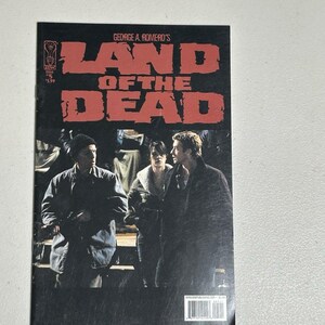 May include: A comic book cover for "George A. Romero's Land of the Dead" featuring three figures in dark coats. The title is in large, red, block letters. The comic book is issue #5.