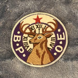 May include: Embroidered patch with a deer design. The patch features a deer with large antlers, a red star, and the letters "B.P.O.E." in a circular design with Roman numerals. The patch has a white border and is on a gray background.